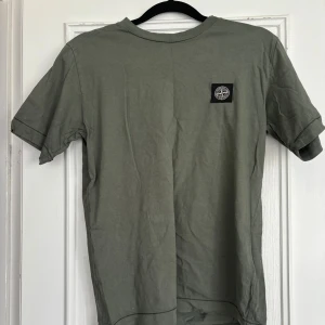 Grön t-shirt från Stone Island - Snygg grön t-shirt från Stone Island med klassisk logopatch på bröstet. T-shirten har rund halsringning och korta ärmar. Perfekt för en avslappnad och stilren look.
