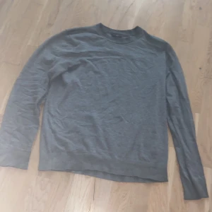 Grå slim fit tröja från H&M - En stilren grå långärmad tröja från H&M i slim fit-modell. Tröjan har rund halsringning och är tillverkad i ett mjukt material som känns skönt mot huden. Perfekt för lager-på-lager och enkel att matcha med andra plagg.