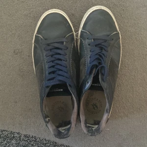 Mörkblå sneakers från Scotch & Soda - Snygga mörkblå sneakers från Scotch & Soda med klassisk design. Skorna har ovandel i skinn och mocka, vita sulor och mörkblå snörning. Märkeslogga på plösen och innersulan. Perfekta för en avslappnad streetstil.