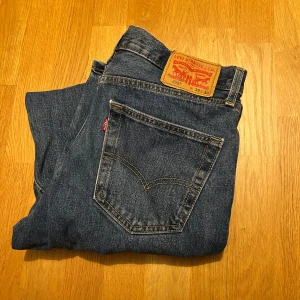 Levi's 550 blå jeans W32 L34 - Klassiska blå Levi's 550 jeans med rak passform och normal midja. Jeansen har fem fickor, Levi's ikoniska läderpatch bak och röd logotagg på bakfickan. Tillverkade i slitstarkt denimtyg av bomull. Perfekta för en avslappnad och tidlös look.