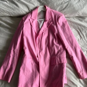 Rosa kavaj - Snygg rosa kavaj med klassisk krage och två fickor framtill. Rak passform och långa ärmar. Perfekt för dig som vill sticka ut med färg. 