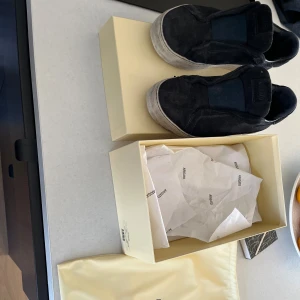 Svarta slip-on sneakers från Axel Arigato - Säljer ett par svarta slip-on sneakers från Axel Arigato i mocka. Skorna har en platt vit sula och minimalistisk design utan snörning. Perfekta för en clean och stilren look. Kommer med originalkartong och dustbag.