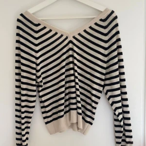 Randig stickad tröja med v-ringning - Snygg stickad tröja med svart och beigea ränder och v-ringad hals. Tröjan har lång ärm och en avslappnad passform. Perfekt för lager-på-lager och passar till både jeans och kjol.