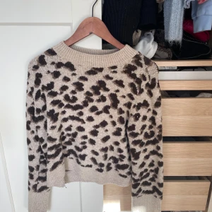 Beige leopardmönstrad stickad tröja - Säljer en beige stickad tröja med leopardmönster i brunt och svart. Tröjan har rund halsringning, ribbade muddar och lång ärm. Perfekt för dig som vill sticka ut lite extra i höst och vinter!