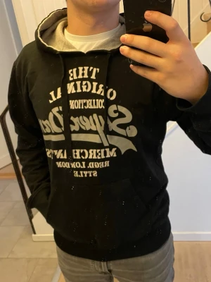 Svart Superdry hoodie med tryck - Svart hoodie från Superdry med stort vitt tryck på bröstet och klassisk känguruficka. Huvan är fodrad i grått och har dragsko. Perfekt för en avslappnad och cool stil. Materialet känns mjukt och bekvämt.