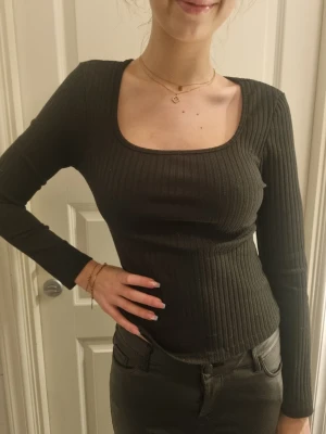 Svart ribbad långärmad topp - Snygg svart ribbad topp med lång ärm och fyrkantig ringning. Toppen har en tight passform och är perfekt att styla med både jeans och kjol. Materialet känns mjukt och stretchigt, vilket gör den bekväm att bära hela dagen. Tyvärr finns inte lappen i nacken kvar men den är i Small.