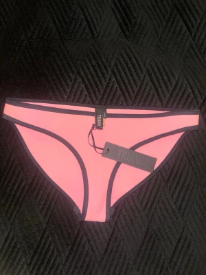 Rosa bikiniunderdel från Triangl - Säljer en rosa bikiniunderdel från Triangl med svarta kanter. Tillverkad i neopren för en sportig och modern look. Perfekt för strand eller poolhäng. Enkel och stilren design som ger en snygg kontrast mellan färgerna. Säljs inte längre, sitter lika bra som M❤️ 