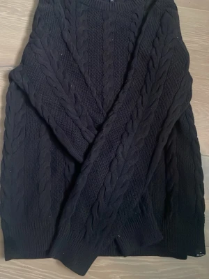 Svart kabelstickad tröja Tommy Hilfiger - Kabelstickad svart tröja från Tommy Hilfiger med klassiskt mönster och ribbade muddar. Perfekt för dig som gillar en stilren och tidlös look. Tröjan har rund halsringning och är mjuk och skön att bära.