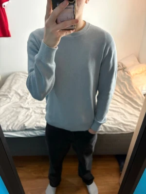 Ljusblå stickad tröja - En stilren ljusblå stickad tröja med rund hals och långa ärmar. Tröjan har en enkel och klassisk design med ribbade muddar vid ärmslut och nederkant. Perfekt för lager-på-lager och passar till många olika outfits knappt använd.