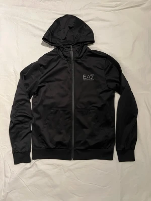 Armani Hoodie, Storlek M - Emporio Armani Kofta för män. Plagget är i storlek M, väldigt bra skick inga skador/slitage.  Snygg diskret monogram på sidan av armen. Hör av er vid intresse/frågor. PRIS KAN DISKUTERAS!
