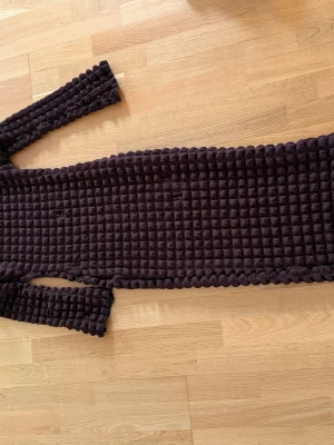 Brun långärmad klänning Boohoo - Långärmad brun klänning från Boohoo med unik quiltad struktur. Klänningen är lång och har en kroppsnära passform. Materialet är mjukt