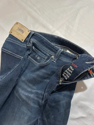 Mörkblå jeans från trammarossa - Snygga mörkblå jeans från trammarossa CD-logga på myntfickan och metallbricka bak. Jeansen har kontrastsömmar och diskret tvätt för en modern look. Perfekta för dig som gillar exklusiva märken och stilren design. Modelen är Leonard slim