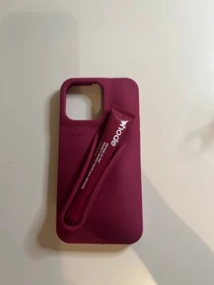 Vinrött mobilskal från rhode  - Snyggt vinrött mobilskal från rhode med smart fack på baksidan, perfekt för att förvara t.ex. läppglans eller småsaker. Skalet är gjort i mjukt silikonmaterial och har en modern, stilren design med rhode-logga. Passar bra 