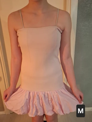 Ljusrosa kort klänning med volang - Söt ljusrosa kort klänning och volang nedtill. Klänningen har en rak, enkel överdel och en utställd kjol som ger en lekfull känsla. Perfekt för varma dagar och somriga tillfällen. Storleken är mer som S