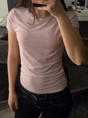 Ljusrosa basic t-shirt från Gina Tricot  - En enkel och stilren ljusrosa t-shirt med rund hals och korta ärmar. Perfekt att matcha med jeans eller kjol för en clean look. Tillverkad i mjukt material som känns skönt mot huden.