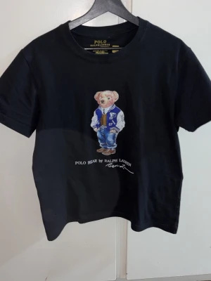 Svart Polo Bear t-shirt Ralph Lauren - Svart t-shirt från Polo Ralph Lauren med ikoniska Polo Bear-trycket på bröstet. Modellen är slim fit och har rund hals samt korta ärmar. Tillverkad i mjuk bomull för skön känsla. Perfekt för dig som gillar klassisk streetstyle med en twist.