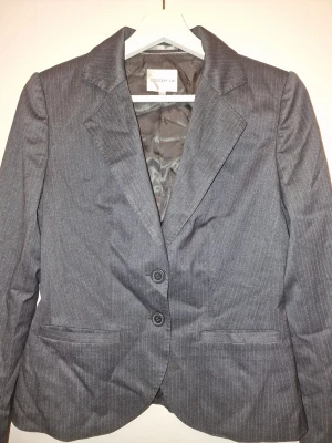 Grå kavaj med matchande kostymbyxor - Stilren grå kavaj i klassisk modell. Perfekt för en stilren och modern look. Kavajen är oanvänd och byxorna använda ca 3-5 gånger.