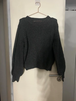 Mörkgrå stickad tröja med rund hals - Mysig mörkgrå stickad tröja med rund hals och långa ärmar. Tröjan har en något boxig passform och ribbstickade muddar vid ärmslut och nederkant. Perfekt för lager på lager och enkel att matcha med olika stilar. Storlek L passar även M. Använd 1-2 gånger