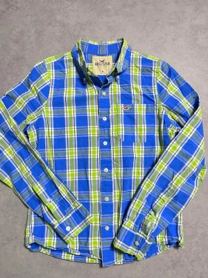 Blå och grön rutig skjorta Hollister - Snygg rutig skjorta från Hollister i blått, grönt och vitt. Skjortan har klassisk krage, knäppning framtill och lång ärm. Perfekt för dig som gillar en avslappnad men ändå stilren look.