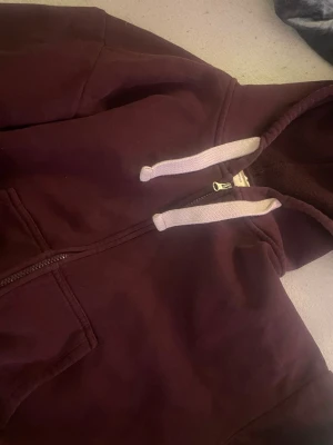 Vinröd hoodie från Gina Tricot - Mysig vinröd hoodie från Gina Tricot med dragkedja, huva och vita snören. 