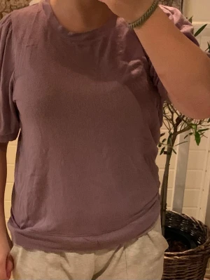 Ljuslila topp med puffärm - Säljer en ljuslila topp med puffärmar och rund halsringning. Toppen har en avslappnad passform och är gjord i mjukt bomullsliknande material. Perfekt för dig som gillar en enkel men trendig stil.