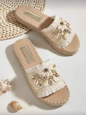 Beige tofflor med snäckor och pärlor - Ena sulan är nedtryckt, skriv privat så skickar jag bild! Trendiga beige sandaler med flätad sula och bred rem i tyg. Dekorerade med snäckor, pärlor och glittriga stenar för en bohemisk vibe. Remmen har fransiga kanter och sandalerna har öppen tå. Perfekta för sommaren och strandhäng. 