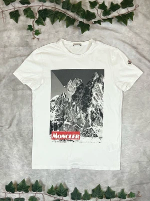 Moncler Maglia T-Shirt – White – Strl M - |Färg: Vit, grafiskt tryck i svart/grått med röd logotyp | Modell: Maglia T-Shirt | Storlek: M, normal passform | Skick: Grade A, 10/10 | Hör av dig ifall du har funderingar!