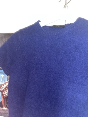 Kornblå stickad kortärmad tröja - En kornblå stickad tröja med korta ärmar och rund hals. Tröjan har ribbade muddar vid ärmslut och nederkant. Materialet är  mjukt och sitter på bra, ull tröja.