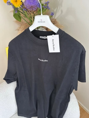 Svart t-shirt från Acne Studios - Svart t-shirt från Acne Studios med klassisk passform och rund hals. Diskret vit logotyp broderad på bröstet. Tillverkad i mjuk bomull som känns skön mot huden. Perfekt basplagg för en stilren och enkel look.