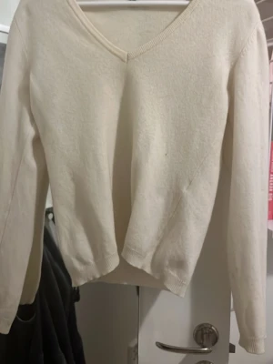 Beige v-ringad stickad tröja Benetton - Krämfärgad stickad tröja från Benetton med v-ringning och långa ärmar. Tröjan har en enkel, klassisk design med ribbade muddar vid ärmslut och nederkant. Ny pris 900 har tyvärr ett jätte litet hål på framsidan  som knappt syns. 