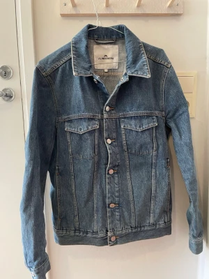 Blå jeansjacka från J.Lindeberg - Klassisk blå jeansjacka från J.Lindeberg med raka linjer, bröstfickor med lock och knappar framtill. Jackan har en tidlös design och är tillverkad i denim med normal passform och långa ärmar.