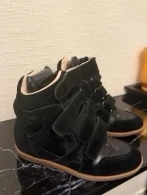 Isabel Marant - Snygga svarta high top sneakers med kardborreband och gummisula. Skorna har en cool design med paneler i mocka och läder samt kontrasterande ljus insida. Perfekta för dig som vill sticka ut med en unik och trendig look.