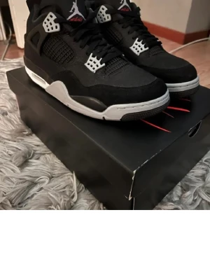 Svarta Air Jordan 4 Retro sneakers - Snygga Air Jordan 4 Retro sneakers i svart med grå och vita detaljer. Skorna har klassisk meshpanel, synlig Air-sula och ikoniska plastdetaljer vid snörningen. Perfekta för dig som gillar streetwear och vill sticka ut med en tidlös modell.