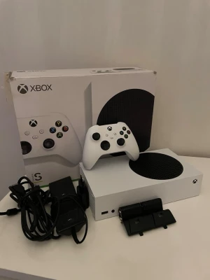 Xbox Series S spelkonsol med tillbehör - Hej jag säljer en Xbox series s som funkar utmärkt utan några problem det ör bara att starta den och spela och som ni ser i bilden så följer det med en Xbox och en kontroll och den orginala kartong och det följer med en laddningstation för kontrollen och som ni ser så följer det med två batterier som används till kontrollen om laddningen tar slut det är bara att lägga den i laddningstationen och den blir fulladdad om du är intresserad elelr har några frågor tveka inte att skriva!