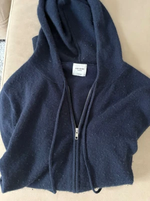 Mörkblå cashmere hoodie John Henric - Mysig mörkblå hoodie från John Henric i lyxig cashmere. Hoodien har dragkedja framtill, huva och dragsko. Perfekt för dig som vill ha något både stilrent och bekvämt. Klassisk modell som passar till det mesta. Den är i bra skick förutom att den har ett litet hål i armhålan och att den är lite luddig. Kom med bud och frågar. Allt är intressant!