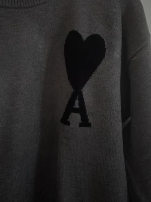 Grå stickad tröja Ami Paris - Säljer en grå stickad tröja från Ami Paris med det ikoniska hjärta-A-motivet på bröstet. Tröjan har rund halsringning och långa ärmar. Perfekt för dig som gillar stilrena och trendiga plagg med en twist.