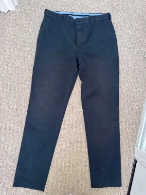 Mörkblå chinos från Brooks Brothers - Snygga mörkblå chinos från Brooks Brothers med klassisk rak passform och bälteshällor. Tillverkade i bomull med en mjuk känsla och ljusblå insida. Perfekta för en clean och stilren look.