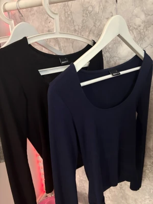 Två tröjor - Säljer två stilrena långärmade toppar från Ginatricot, med en slit på armarna en i svart och en i mörkblått. Båda har rundad urringning och är i mjukt, stretchigt material som sitter snyggt på.  1 för 50kr både för 100kr