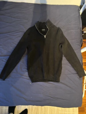 Svart stickad tröja med halv dragkedja - Säljer en svart stickad tröja från only & sons med halv dragkedja och hög krage. Tröjan har lång ärm och ribbstickad struktur som ger en stilren look. Perfekt för lager på lager och enkel att matcha med olika outfits.