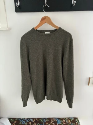 Olivgrön stickad tröja i Kashmir  - En enkel och stilren olivgrön stickad tröja med rund halsringning och långa ärmar. Tröjan har ribbade muddar vid ärmslut och nederkant. Perfekt för lager på lager och passar till det mesta. 100% Kashmir.