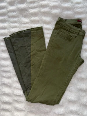 Olivgröna bootcut jeans - Säljer ett par lågmidjade olivgröna jeans i två toner som jag har sytt om själv med symaskin till bootcut. Se bild för inte helt perfekt men har sett till att de inte fransar sig. Har även sytt en söm längst ner för att de inte ska fransa sig. Från märket Mavi. Passar storlek 26-28 i waist och 32 i längd. Stretchigt material