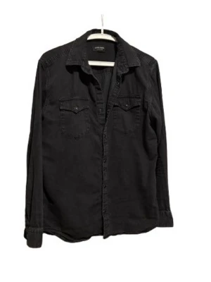 Svart skjorta med fickor från H&M - Stilren svart skjorta från H&M med klassisk krage och två bröstfickor med lock och knappar. Skjortan har långa ärmar och är tillverkad i mjuk bomull. Perfekt för en avslappnad men snygg look.