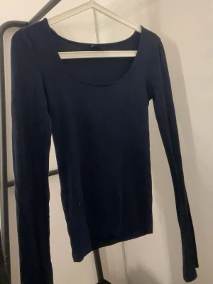 Mörkblå långärmad topp - En enkel och stilren mörkblå långärmad topp med rundad halsringning. Toppen har en tight passform och är perfekt att matcha med jeans eller kjol. Materialet känns mjukt och stretchigt, vilket gör den bekväm att bära hela dagen.
