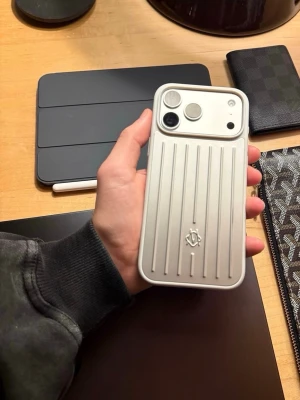 Silverfärgat mobilskal med räfflat mönster - Snyggt mobilskal i silver från RIMOWA med räfflat mönster och logga på baksidan. Skalet är gjort i hårdplast och har en modern, stilren design som ger din mobil en exklusiv look. Perfekt för dig som gillar minimalistisk och lyxig stil.