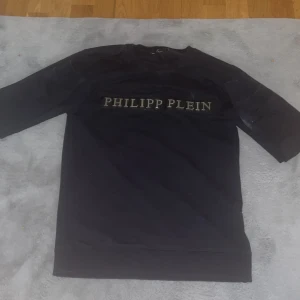 Svart Philipp Plein t-shirt - Snygg svart t-shirt från Philipp Plein med stort logotyp-tryck framtill i silver. Klassisk rund halsringning och normal passform. Perfekt för dig som gillar exklusiva streetwear-plagg.