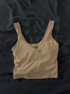 Rosa croppad topp från Lululemon - Snygg croppad topp från Lululemon i strawberry milkshake färgen. Toppen har v-ringning framtill och breda axelband, perfekt för träning eller chill. Tillverkad i mjuk bomullsmix som känns skön mot huden. Enkel och stilren design med liten logga på ryggen.