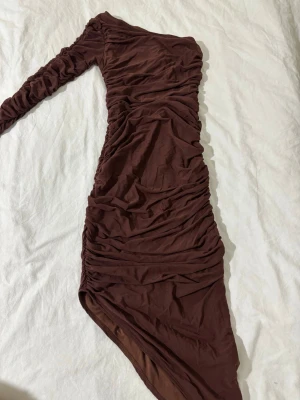 Brun rynkad asymmetrisk klänning🤎 - Brun, figurnära klänning med rynkade detaljer och one shoulder. Stretchigt, mjukt material som sitter tajt och formar kroppen. Perfekt till fest, utgång eller middag. Aldrig använd!❤️❤️