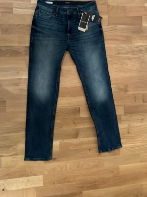 Mörkblå jeans från Jack & Jones - Snygga mörkblå jeans från Jack & Jones med klassisk femficksdesign och lätt slitna detaljer på låren. Jeansen har rak passform och är tillverkade i bomull med en skön stretch. Perfekta för en avslappnad och trendig look.