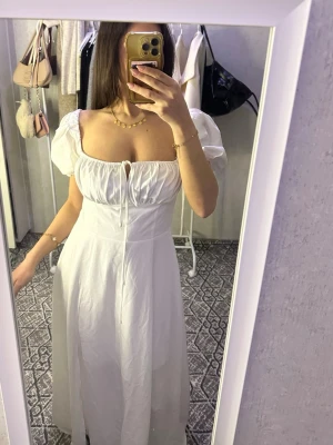 Vit långklänning med puffärmar - Superfin vit långklänning med puffiga ärmar och söt snörning framtill. Klänningen har en romantisk och luftig känsla, perfekt för varma dagar. Den har en smickrande passform och kan bäras både på axlarna och offshoulder.