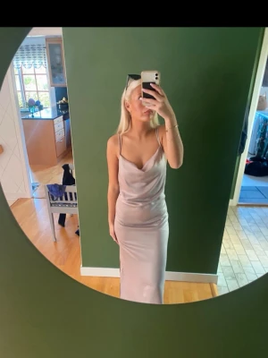 Beige balklänning,brudklänning  - Snygg långklänning i  satin med smala axelband och draperad urringning. Klänningen har en elegant och slimmad passform som ger en stilren look. Perfekt för dig som vill sticka ut med en enkel men trendig stil. Har prislapp kvar 700 ny